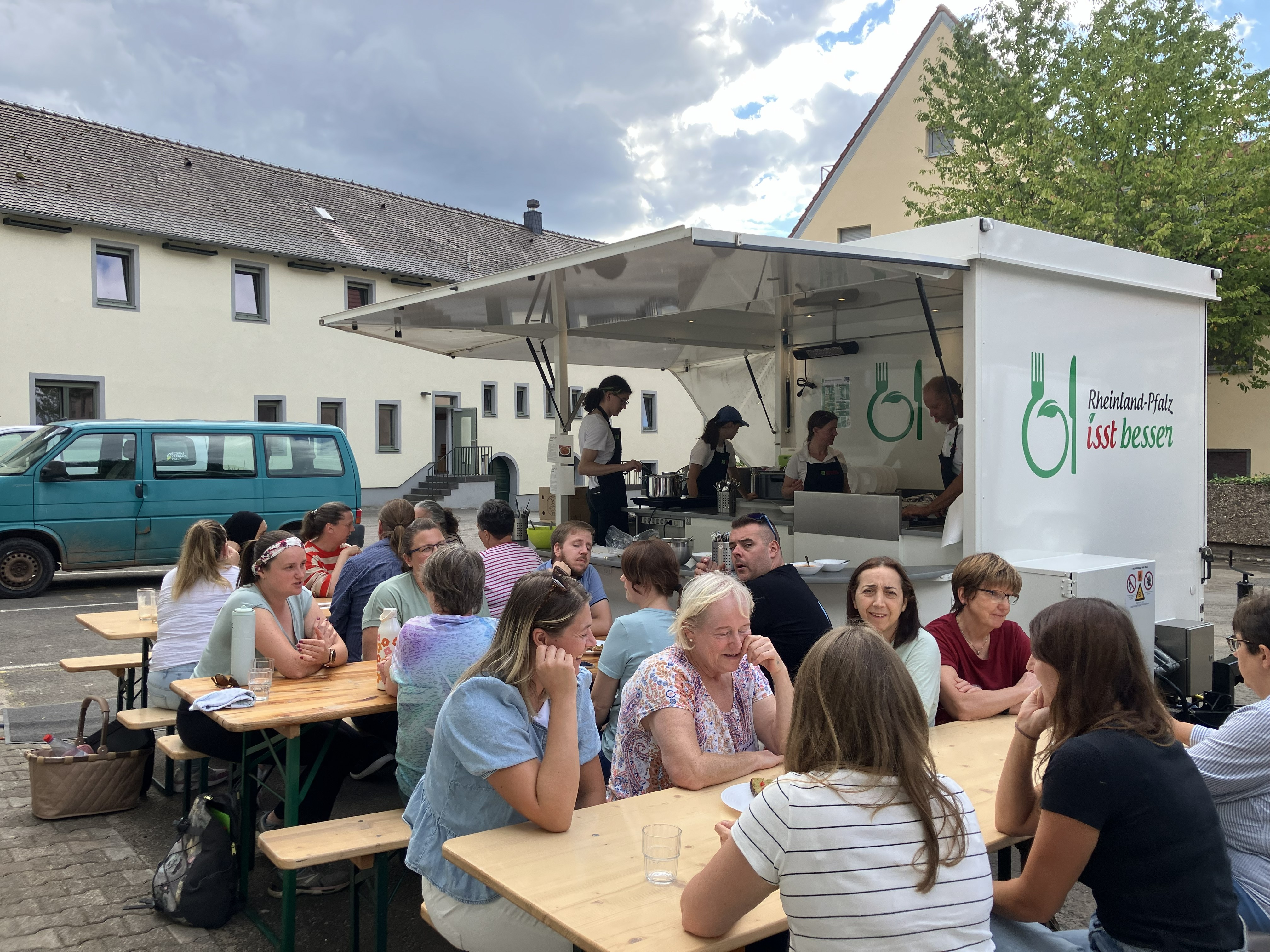 Menschen sitzen an Biergartentischen vor einem Food-Track.