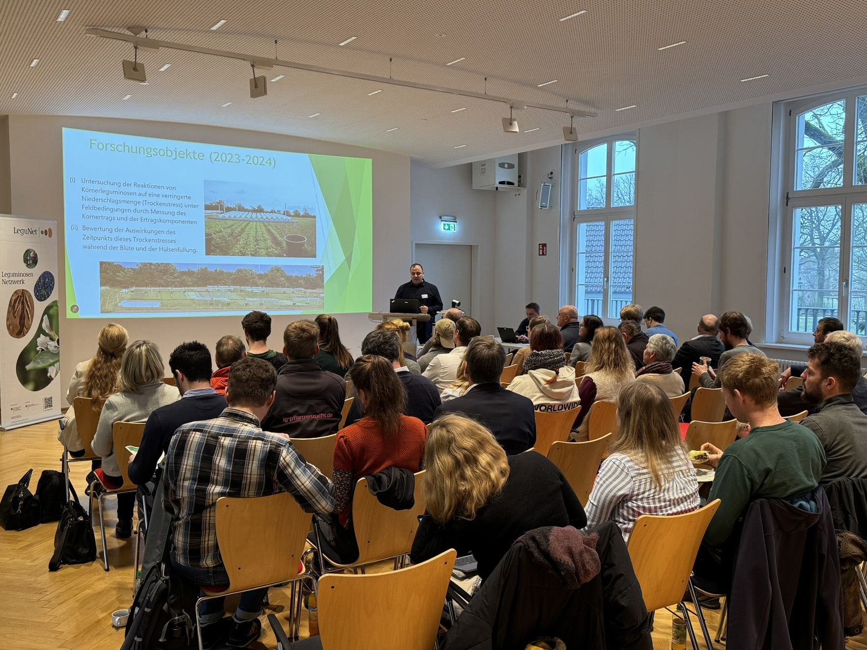 Mann hält eine Präsentation in einem Saal mit Zuhörenden.